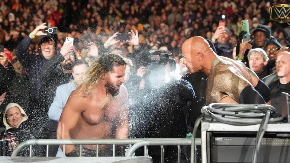The Rock and Cody Rhodes spraying each other with water in front of a crowd.