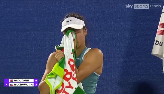 Emma Raducanu wiping her face with a towel after a tennis match.